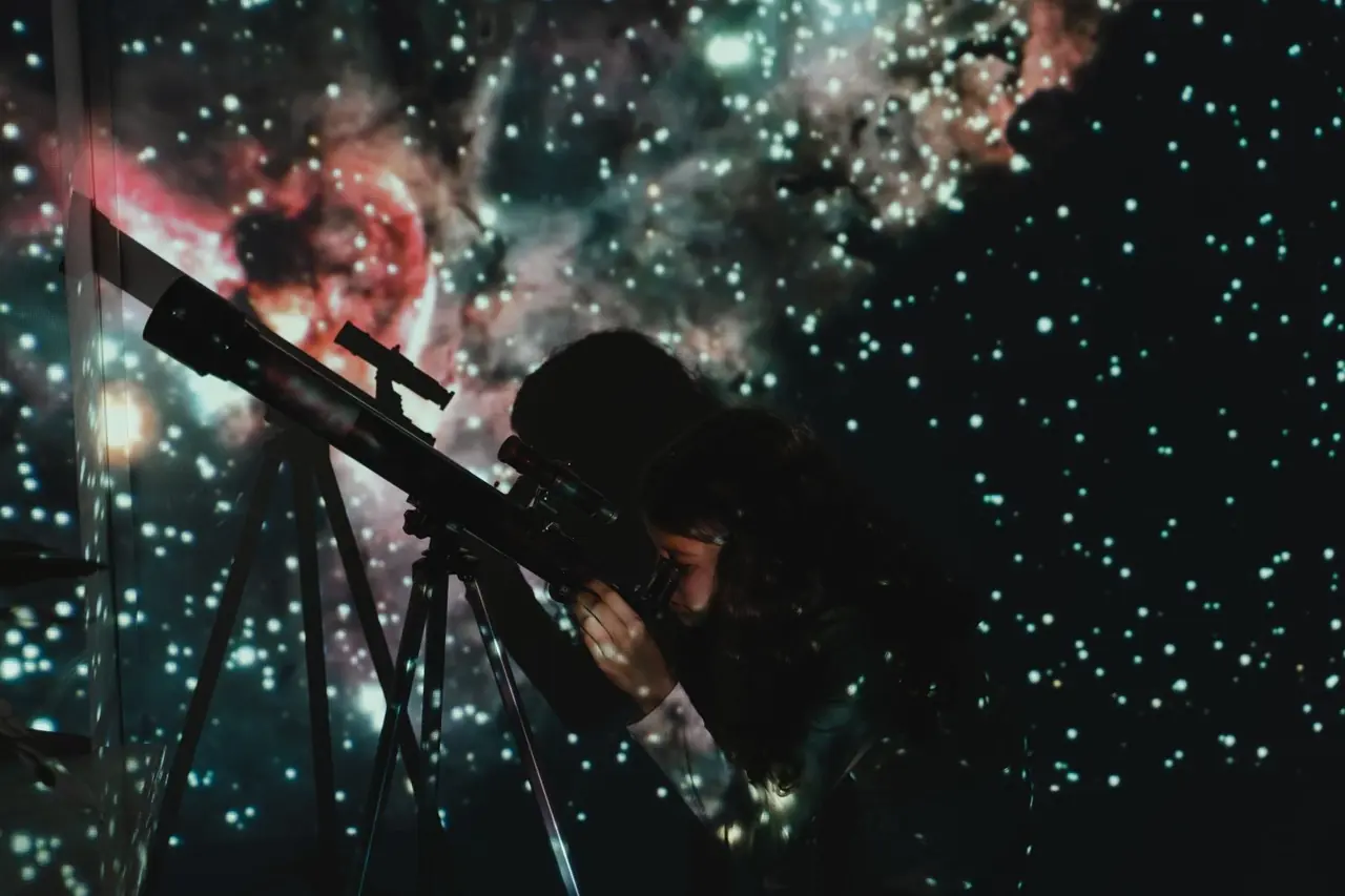 A student looking through a telescope at a star projection